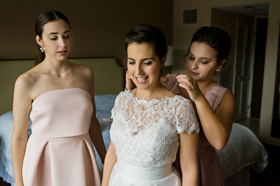 Bridesmaids help the bride put on her necklace during the getting ready part of the wedding day.